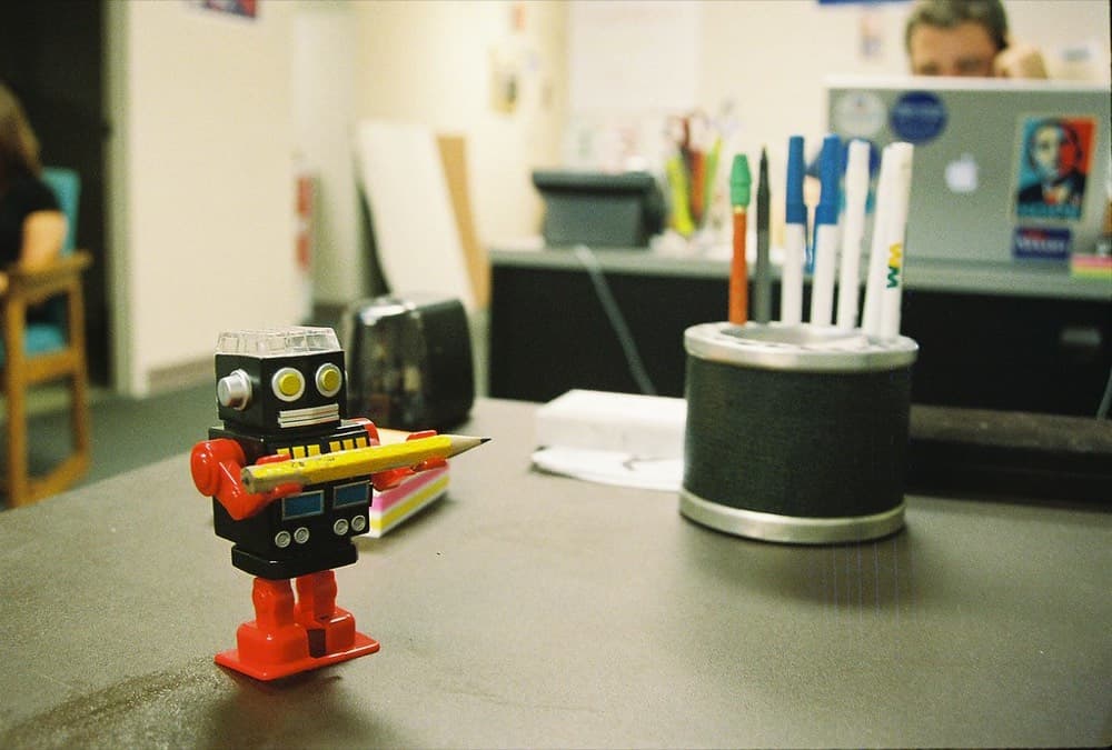 Un petit robot jouet tenant un crayon sur un bureau